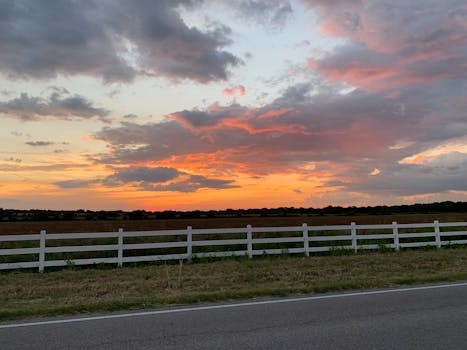 Breathtaking sunset over a Texas pasture with vivid colors and a white fence lining the road.
